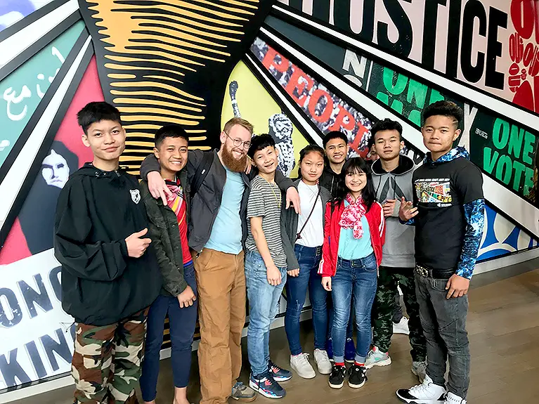 A group of teenagers pose in front of a mural at the Center for Civil and Human Rights.